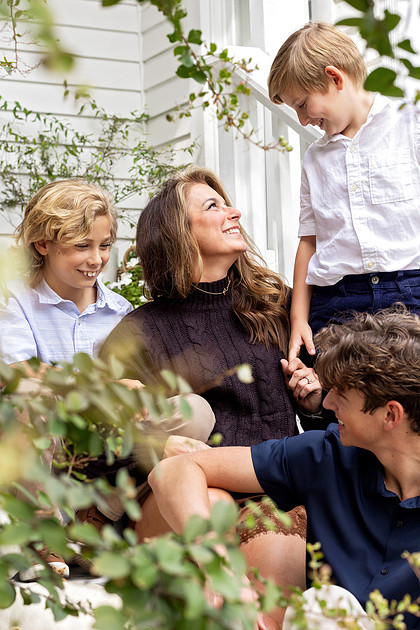 Mother smiling with her three sons on the porch during a fall family photography session at The Beverly-Harris House in McKinney, Texas.
